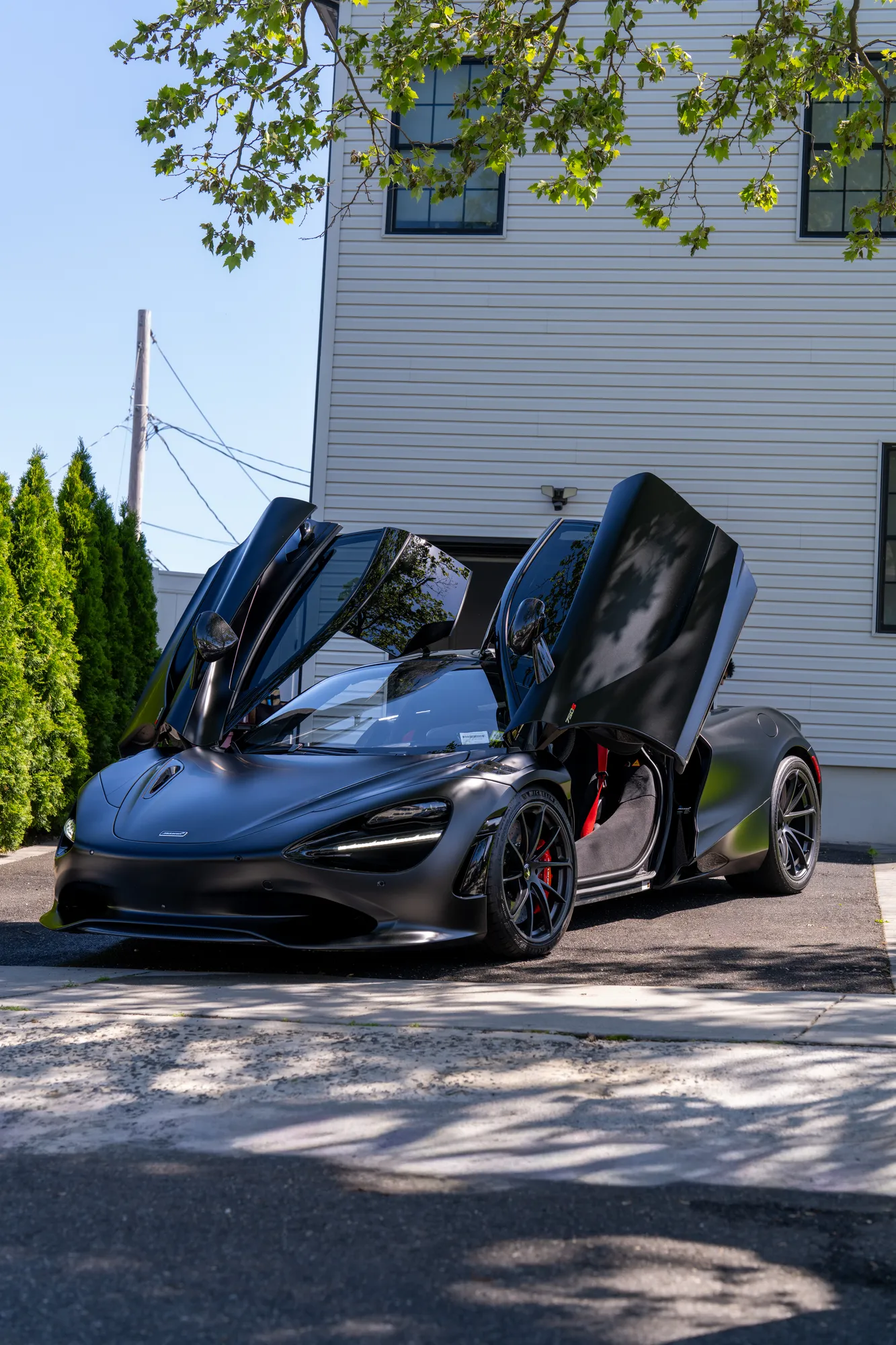 Black McLaren with both doors raised outside a white building